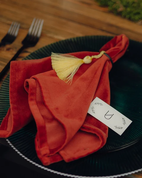 Терракотовая бархатная салфетка с золотистой кисточкой на тёмной тарелке